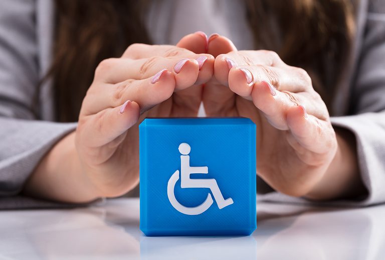 Hands protecting blue block with wheelchair symbol.